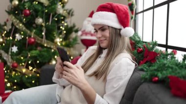 Genç ve güzel İspanyol kadın akıllı telefon kullanıyor. Yılbaşı ağacının yanında oturuyor.