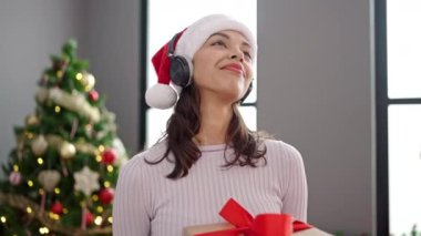Genç ve güzel İspanyol kadın Noel ağacının yanında dans ediyor. Evde kulaklık takıyor.