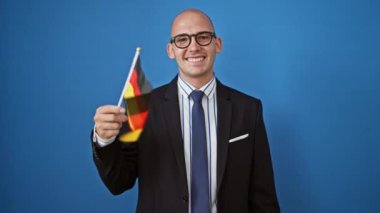 Genç İspanyol iş adamı elinde Alman bayrağı tutarken mavi arka planda gülümsüyor.