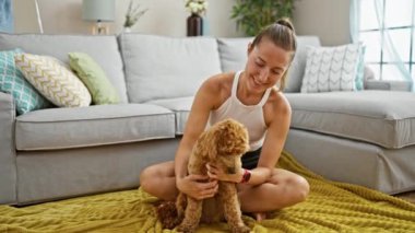 Köpekli beyaz bir kadın evde yerde oturmuş oynuyor.