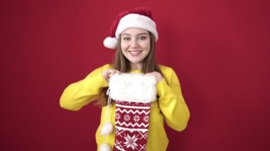 Genç sarışın kadın gülümsüyor. Kırmızı arka planda kendine güvenen bir Noel çorabı tutuyor.