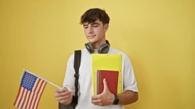 Canlı genç İspanyol öğrenci, umut vadeden bir genç kitaplar ve Birleşik Devletler bayrağı ile, gösterişli günlük yaşam tarzıyla duruyor, hayat dolu sarı bir arka planda izole edilmiş.