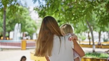 Parkta dans eden neşeli anne, kollarında gülümseyen kızı, güneşi ıslatan, neşe içinde güneşlenen
