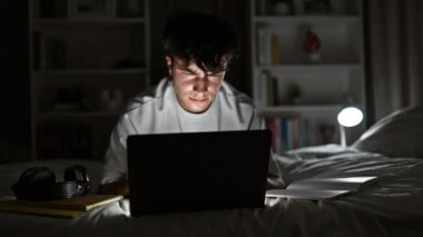 Laptop kullanan genç bir İspanyol yatak odasında ders çalışıyor.