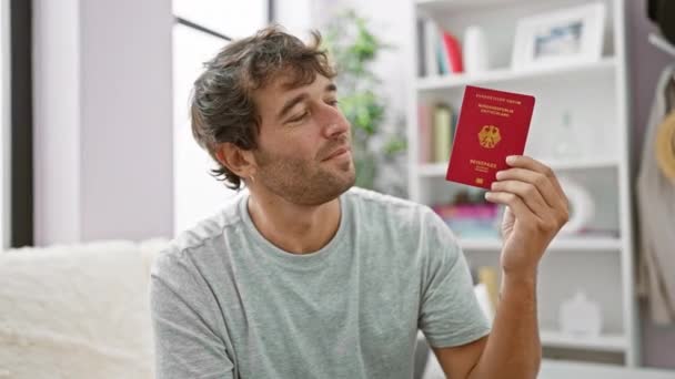 快乐的年轻人 带着他的德国护照 自信地微笑着 懒洋洋地躺在家里的沙发上 准备去欧洲探险 — 图库视频影像