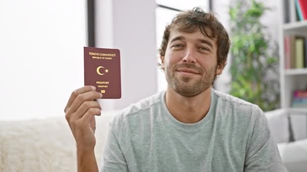 カジュアルな若者は自宅のソファーに座っている間喜びと自信を誇らしげに伝染性の笑顔で彼のトルコのパスポートを表示します — ストック動画