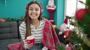 Genç, güzel, İspanyol bir kadın müzik dinliyor. Evde Noel 'i kutlarken kahve içiyor.