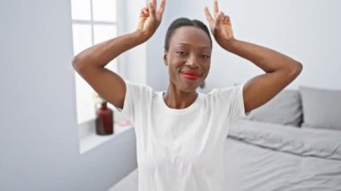 Neşeli Afro-Amerikalı kadın yatakta komik pozlar veriyor tavşan kulaklı jest, odayı neşe ve çılgın bir eğlence ile dolduruyor..