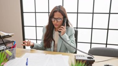 Öfkeli genç İspanyol kadın, güzel ama kızgın, çalışırken ofis telefonunda iş konuşuyor.