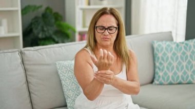 Orta yaşlı İspanyol kadın koltukta oturuyor ve evinde bilek ağrısı çekiyor.