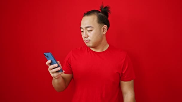 ブタの髪型が大きい若くて幸せな中国人男性は 耳から耳まで笑い 活気に満ちた赤い背景に対して自信を持ってドルと彼の信頼できる携帯電話を保持しています — ストック動画