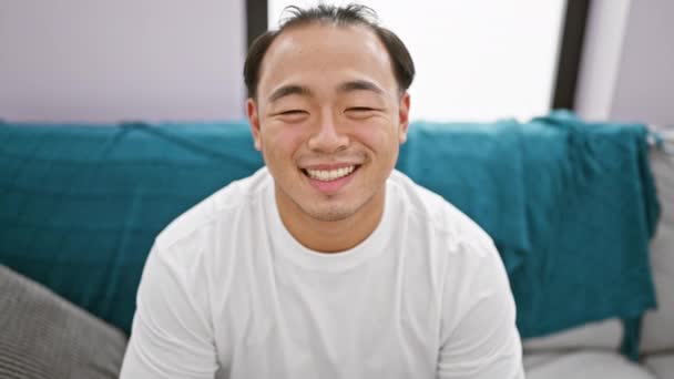 喜びを放射し 若い中国人男性 自信と陽気 家庭で居心地の良いソファーでリラックスし 純粋な幸せと快適さを表現する彼の笑顔 — ストック動画