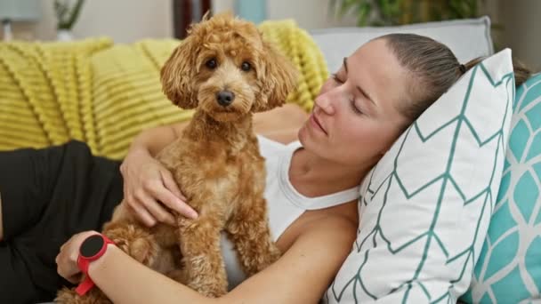 自宅で抱き合うソファーに横たわっている犬を持つ若い白人女性 — ストック動画