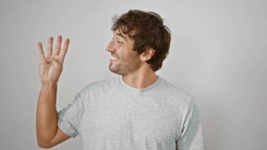 Neşeli genç adam rahatça tişörtünü giyerken büyük bir gülümseme sergiliyor, parmaklarıyla dört numaralı jestini sergiliyor, el değmemiş, izole edilmiş beyaz bir arka plana işaret ediyor..