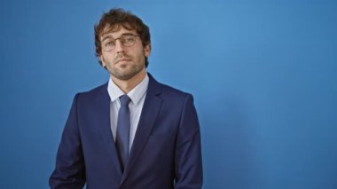 Ciddi bir genç adam, takım elbiseli yakışıklı bir yetişkin, parmağını yana doğru gösteriyor. Kendine güveni tam, sessiz yüzü mavi arka planda izole edilmiş bir reklamı gösteriyor.