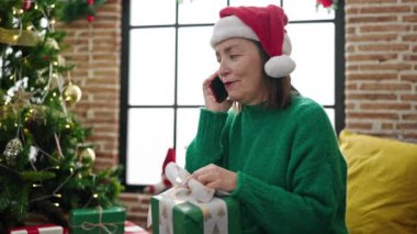 Evde Noel ağacının yanında telefonla konuşan gri saçlı, olgun İspanyol kadın.