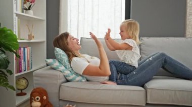 Kafkasyalı anne ve küçük kız rahat koltukta uzanır, el oyunları oynar ve el çırparlar, evlerinin rahat içinde mutlu bir gülümseme paylaşırlar..