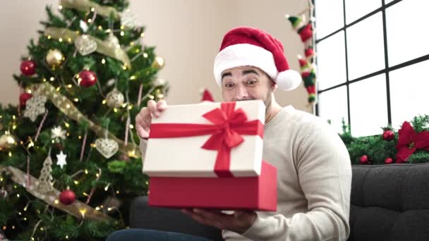 Jovem Hispânico Desembalar Presente Sentado Sofá Pela Árvore Natal Casa — Vídeo de Stock