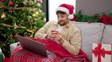 Genç Arap adam film izliyor. Kahve içiyor. Evde Noel ağacının yanında oturuyor.