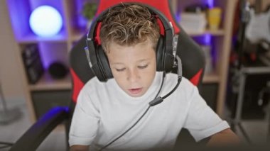 Sevimli sarışın çocuk streamer oyun oynayarak mutlu oluyor, evinde bilgisayar başında oyun oynuyor, kulaklık ve oyun platformunu güvenle kullanıyor.