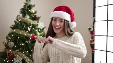 Genç ve güzel İspanyol kadın Noel ağacının yanında durmuş evde dans ediyor.