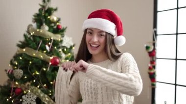 Genç ve güzel İspanyol kadın Noel ağacının yanında durmuş evde dans ediyor.