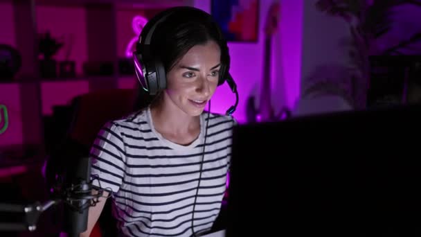 若く美しいヒスパニックの女性は自信を持ってフレンドリーな笑顔で彼女のビデオゲームをロックし ダークゲームルームで ジェスチャーを点滅 — ストック動画