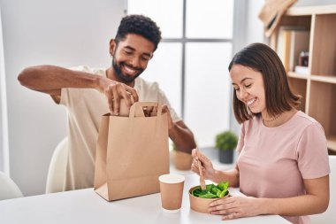 Man and woman couple sitting on table eating take away food at home