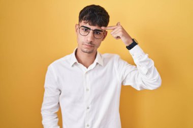 Sarı arka planda duran genç İspanyol adam alnındaki sivilceden mutsuz olduğunu gösteriyor, siyah başlıktaki çirkin enfeksiyon. sivilce ve deri problemi 