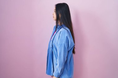 Pembe arka planda duran genç Asyalı kadın yan tarafa bakıyor, rahat poz veriyor doğal bir yüzü ve kendine güvenen bir gülümsemesi var.. 