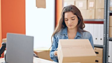 Genç ve güzel İspanyol kadın ecommerce iş adamı. Ofiste akıllı telefonlu bir paket tarıyor.