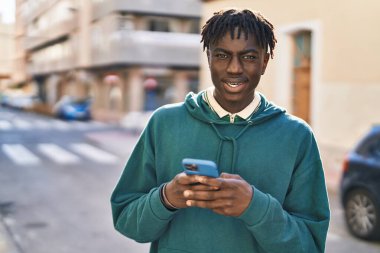 Sokakta akıllı telefon kullanan, kendinden emin gülümseyen Afrikalı Amerikalı bir adam.
