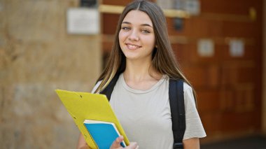 Sırt çantası takan güzel bir kız öğrenci okulda kitap tutuyor.