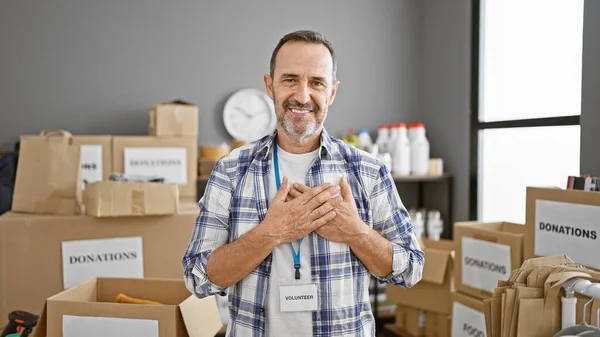 stock image Confident grey-haired middle-aged man standing with heart filled hands, smiling as a volunteer in his community charity center