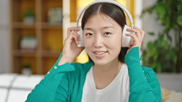 Young chinese woman listening to music sitting on sofa at home