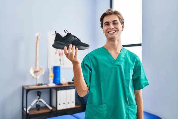 在理疗诊所工作的年轻人 手握鞋子 面带微笑 面带微笑 面带微笑 看上去很积极 很快乐 — 图库照片