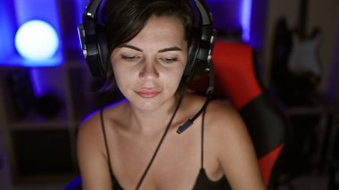 Sersemletici genç İspanyol kadın flaması, ciddi bir yüzle bir oyun deresine dalmış, oyun odasında kulaklıklarla aksesuar takmış..