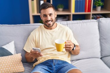 Genç İspanyol adam akıllı telefon kullanıyor. Evde kahve içiyor.