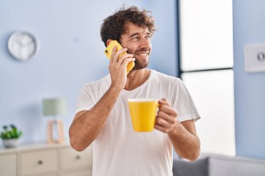 Genç adam akıllı telefonda konuşuyor. Evde kahve içiyor.