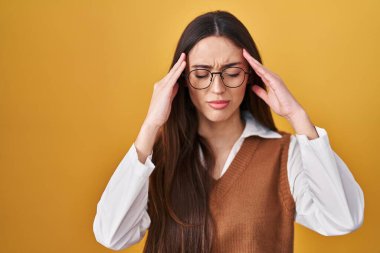 Sarı arka planda duran genç esmer kadın. Stres yüzünden eli başının üstünde gözlük takıyor. migren ağrısı. 