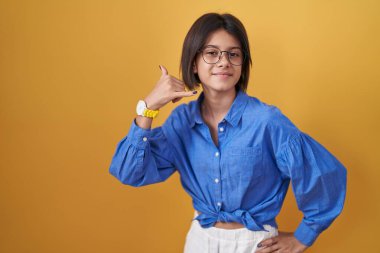 Sarı arka planda duran genç kız gülümsüyor telefonla el ve parmaklarıyla jest yapıyor telefonda konuşuyor gibi. iletişim kavramları. 