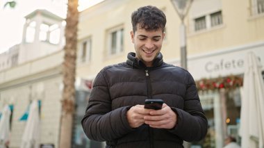 Kafe terasında gülümseyen akıllı telefon kullanan genç bir İspanyol.