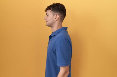 Sarı arka planda dikilen İspanyol genç adam yan bakıyor, rahat poz veriyor doğal bir yüz ve kendine güvenen bir gülümsemeyle.. 