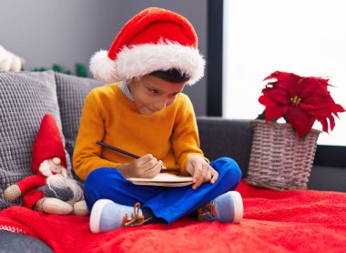 Sevimli İspanyol çocuk Noel şapkası takıp eve Noel Baba mektubu yazıyor.