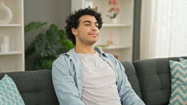 Evdeki kanepede kendinden emin gülümseyen genç latin adam.