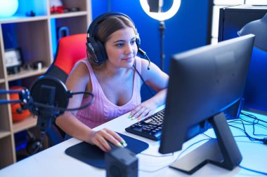 Young beautiful hispanic woman streamer playing video game using computer at gaming room