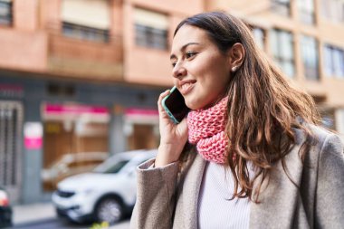 Young beautiful hispanic woman talking on smartphone wearing scarf at street