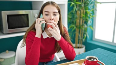 Genç İspanyol kadın kahvaltı yapıyor. Yemek odasında akıllı telefondan konuşuyor.