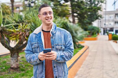 Parkta akıllı telefon kullanarak gülümseyen İspanyol genç adam.