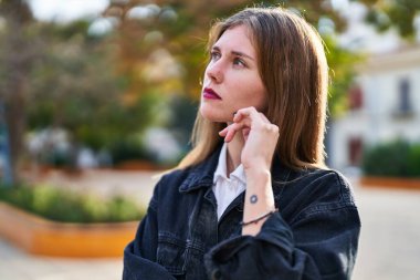 Young blonde woman standing with doubt expression at park